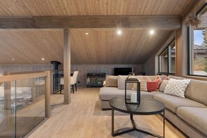 Um amplo loft com pé direito alto, área de jantar, conjunto de sofás e uma grande janela com vista.