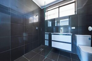 Un bagno moderno con piastrelle scure, cabina doccia in vetro e lavabo doppio.