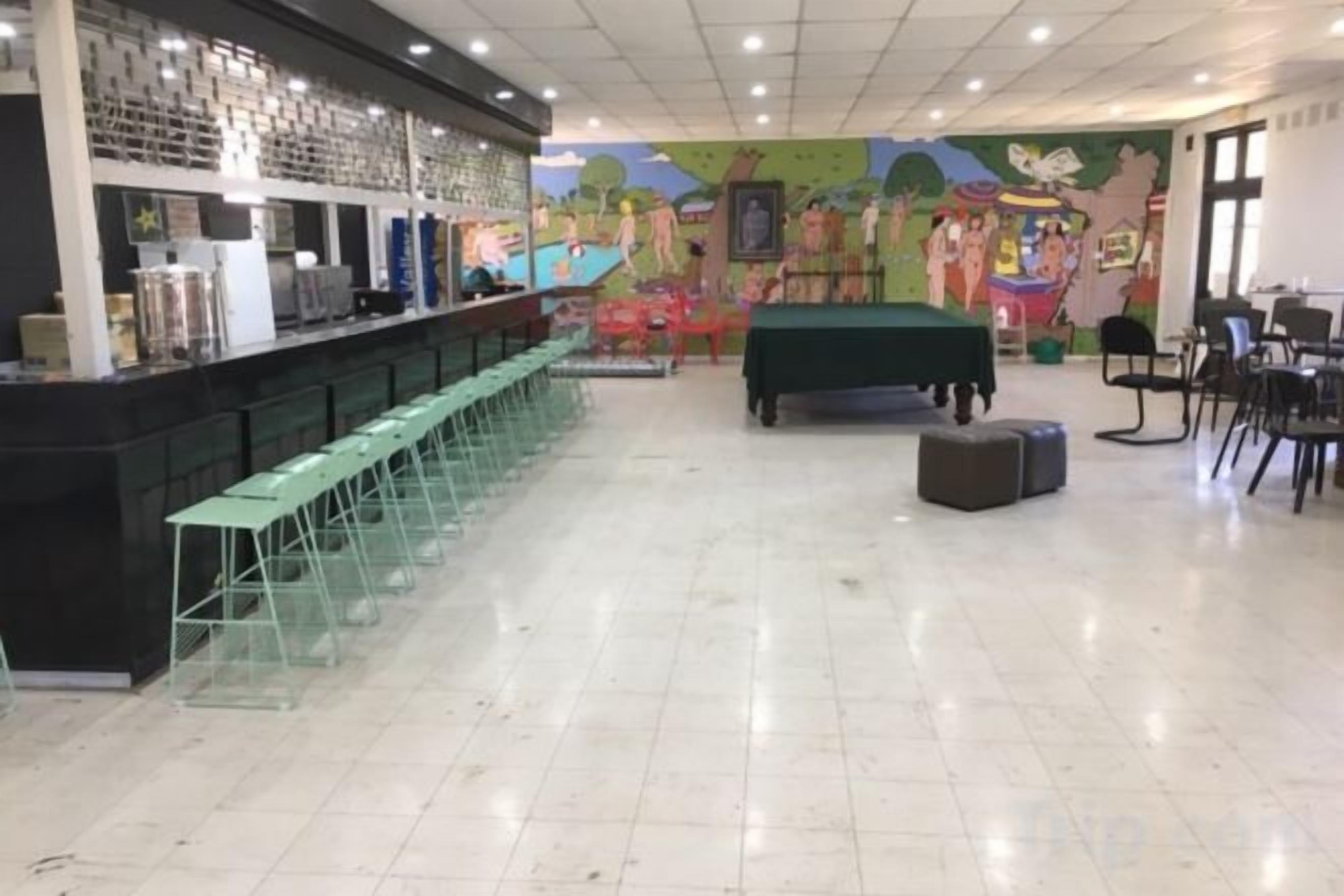 Zona de bar con una barra larga y varios taburetes, una mesa de billar y un mural en la pared.