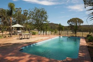 A rectangular swimming pool with a paved deck, surrounded by a fence, trees, and a small gazebo with chairs. - Thoona Eco Resort (Thoona)