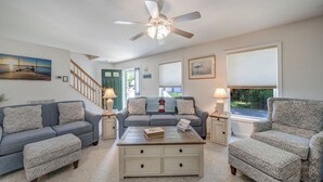 A living room with a sofa, two armchairs, a coffee table, a ceiling fan, and a staircase. - Sundance by Seaside Vacations & Sales (Chincoteague Island)