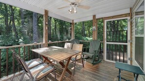 A wooden deck with a table and chairs, surrounded by glass doors and windows offering a forest view. - Sundance by Seaside Vacations & Sales (Chincoteague Island)