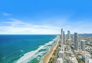 A coastal cityscape with high-rise buildings, a beach, and a clear blue sky.