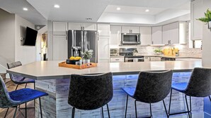 A modern kitchen with a central island, stainless steel appliances, and blue bar stools. - Elegant Hillside Estate | Heated Pool+Sunset Views (El Cajon)