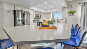 A modern kitchen with white cabinets, stainless steel appliances, and a large island with blue chairs. - Elegant Hillside Estate | Heated Pool+Sunset Views (El Cajon)