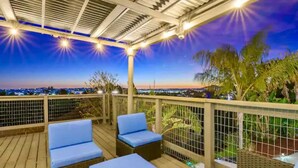 An outdoor deck with wicker furniture and a view of the city at dusk. - Elegant Hillside Estate | Heated Pool+Sunset Views (El Cajon)