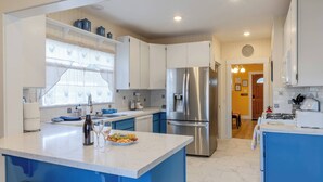 A modern kitchen with white and blue cabinetry, stainless steel appliances, and a marble countertop. - 2 Streets to the Beach! Game Room BBQ & Firepit (Seaside)