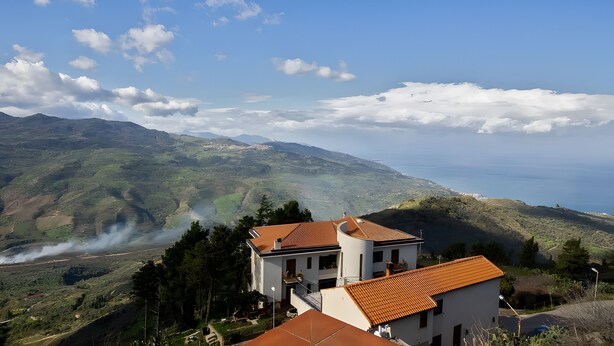 Une maison avec un toit rouge, entourée de verdure et de collines, qui offre une vue sur la côte.