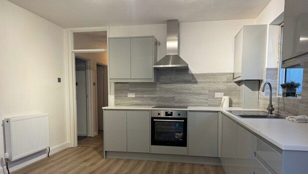 A modern kitchen with a built-in oven, stainless steel range hood, and a large window above the sink.