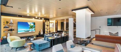 A modern living room with a large flat-screen TV, comfortable seating, and a staircase leading to an upper level.