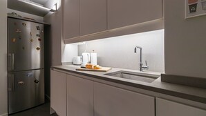 Une cuisine moderne équipée d’un réfrigérateur en acier inoxydable, d’un four encastré, d’un évier avec un robinet, et d’un plan de travail agrémenté d’une planche à découper et d’un pain.