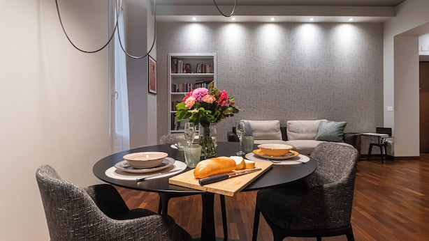 Un espace repas moderne avec une table ronde, des chaises, un vase de fleurs et une bibliothèque en arrière-plan.