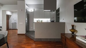 Une cuisine moderne avec des meubles gris, un four encastré et un îlot central. On y trouve également un coin repas avec une table et des chaises en bois.