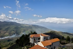 A house with a red roof, surrounded by greenery and hills.