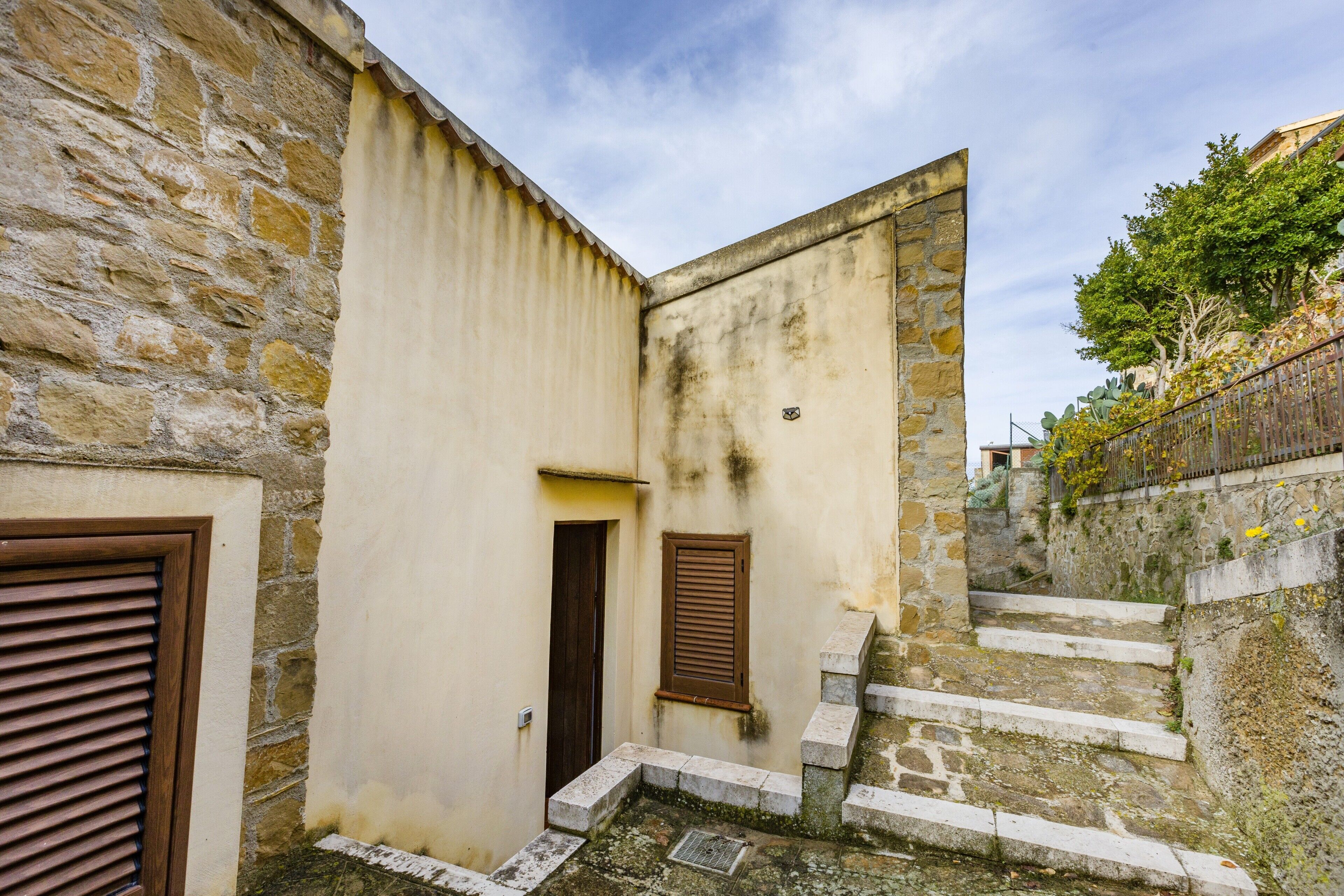 A narrow alleyway with stone walls, a wooden door, and a small window with shutters.