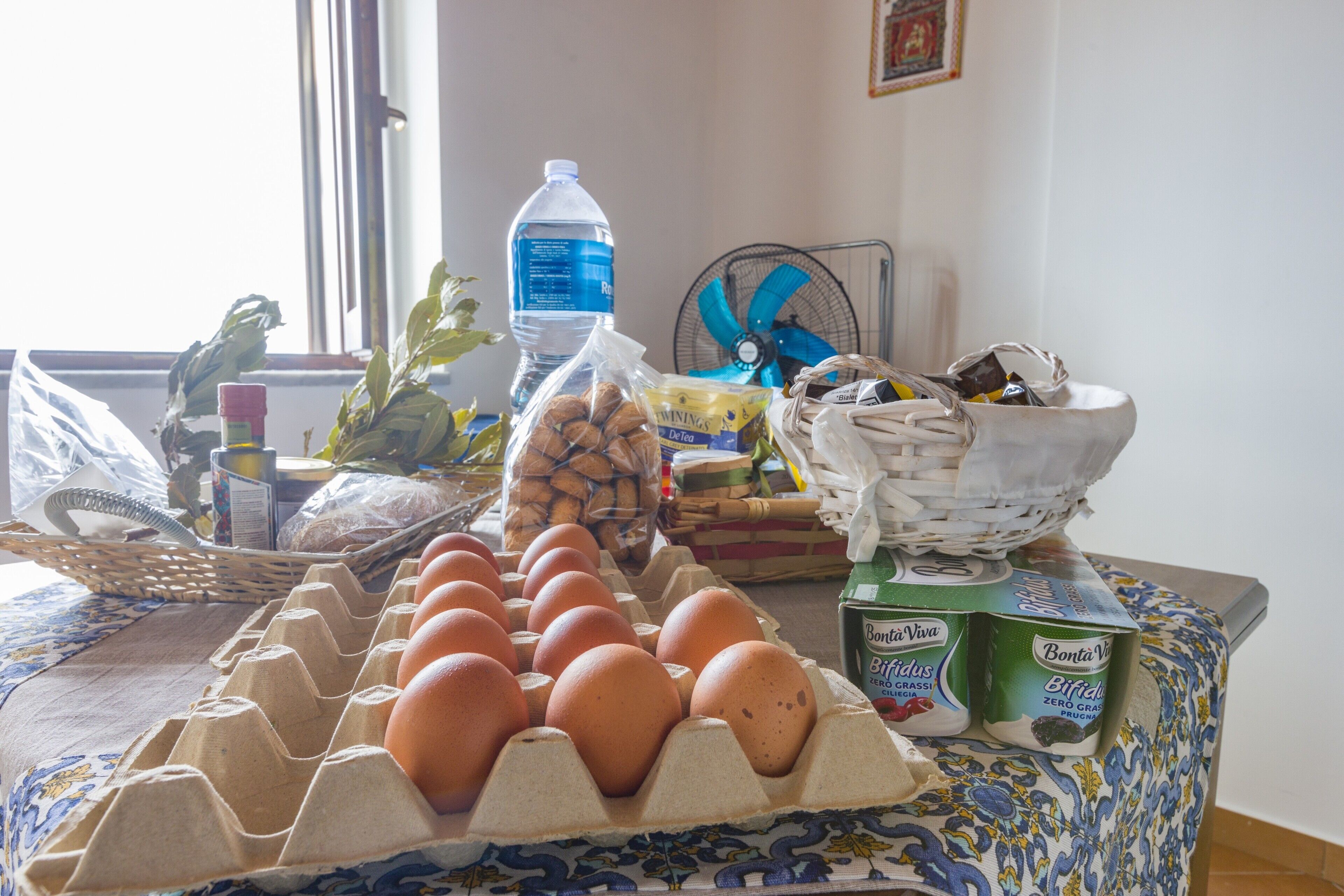A kitchen counter with eggs, a water bottle, a fan, and a basket of bread.