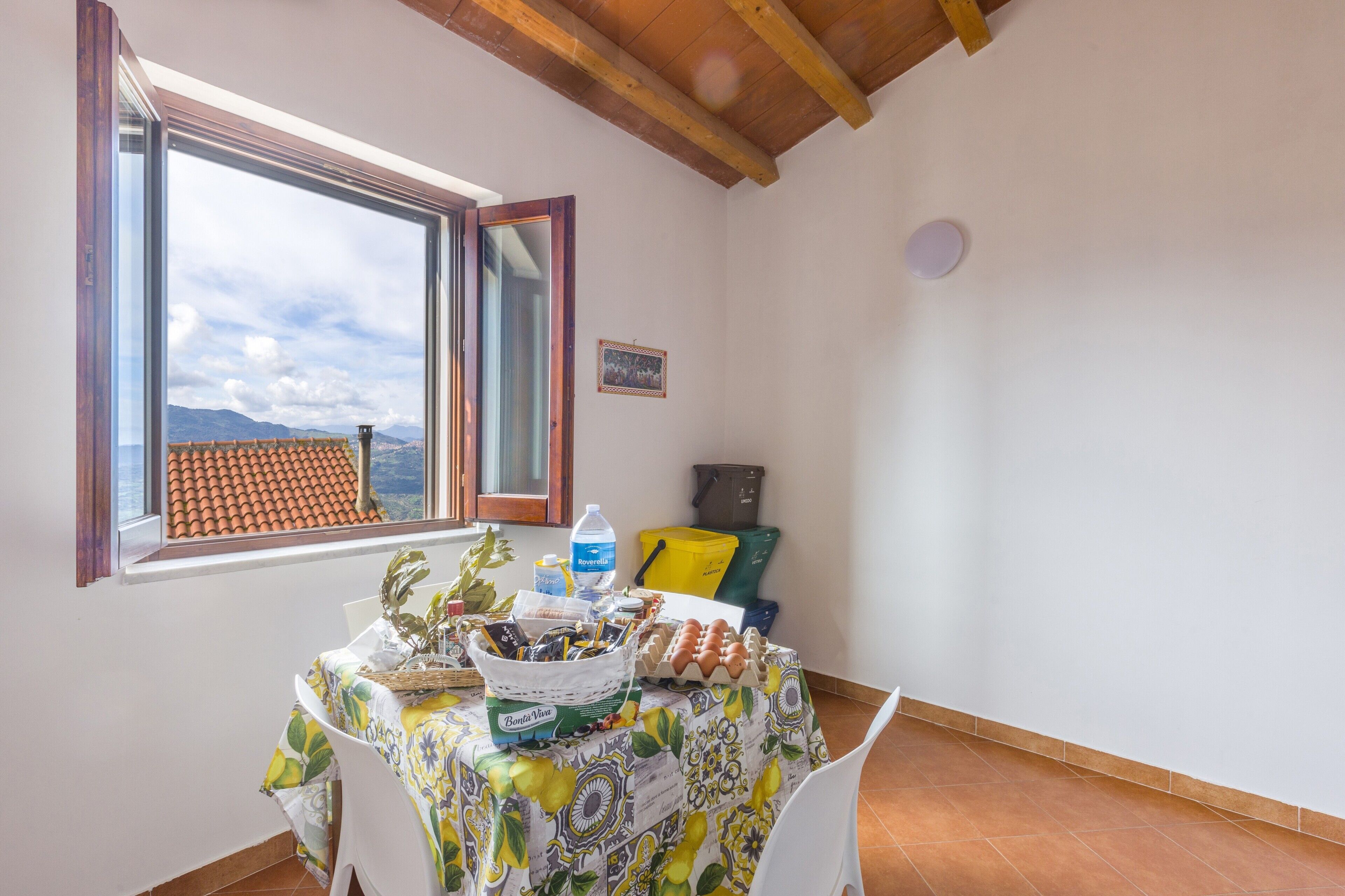 Zona pranzo con tavolo apparecchiato per la colazione, una finestra vista montagne e un soffitto in legno.