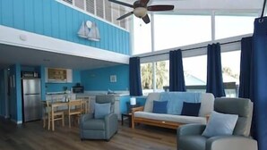 Un espace de vie comprenant un canapé, des fauteuils, une table à manger et une cuisine en arrière-plan.