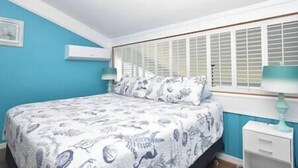 Une chambre à coucher avec un lit, une fenêtre avec des volets, une table de chevet et une lampe.
