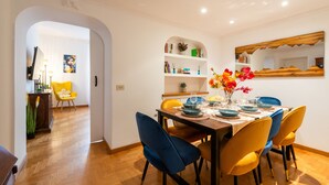 A dining area with a wooden table, blue and yellow chairs, and a vase of flowers. - Piazza del Popolo Brunetti apartment (Roma)