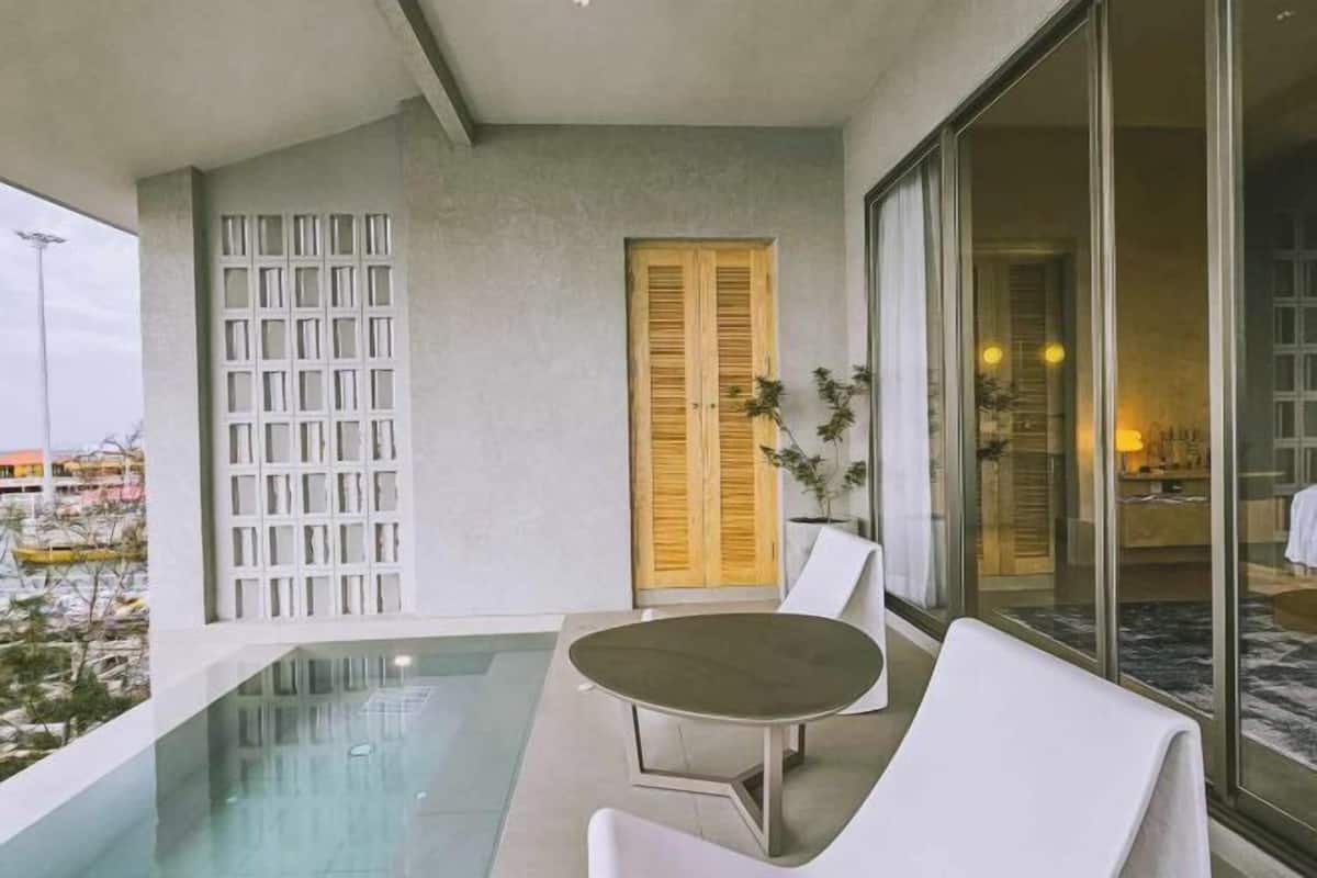 Une chambre d’hôtel moderne dotée d’un balcon en verre, d’une porte en bois et offrant une vue sur le paysage urbain.