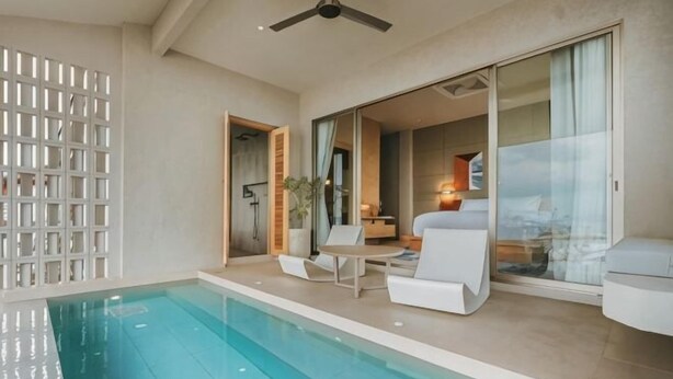 Una piscina con ventilador de techo, un área de estar exterior blanca y vista al interior.