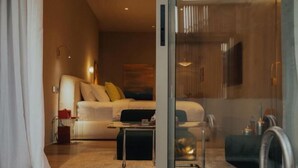 Una habitación de hotel moderna con sofá, una mesa de centro y una pared divisoria de vidrio.