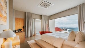 Una habitación de hotel moderna con una cama grande, un escritorio con lámpara, vistas a la ciudad y un balcón.