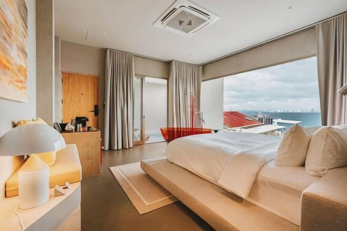 Une chambre d’hôtel moderne dotée d’un grand lit, d’un bureau avec une lampe, d’une vue sur la ville et d’un balcon.