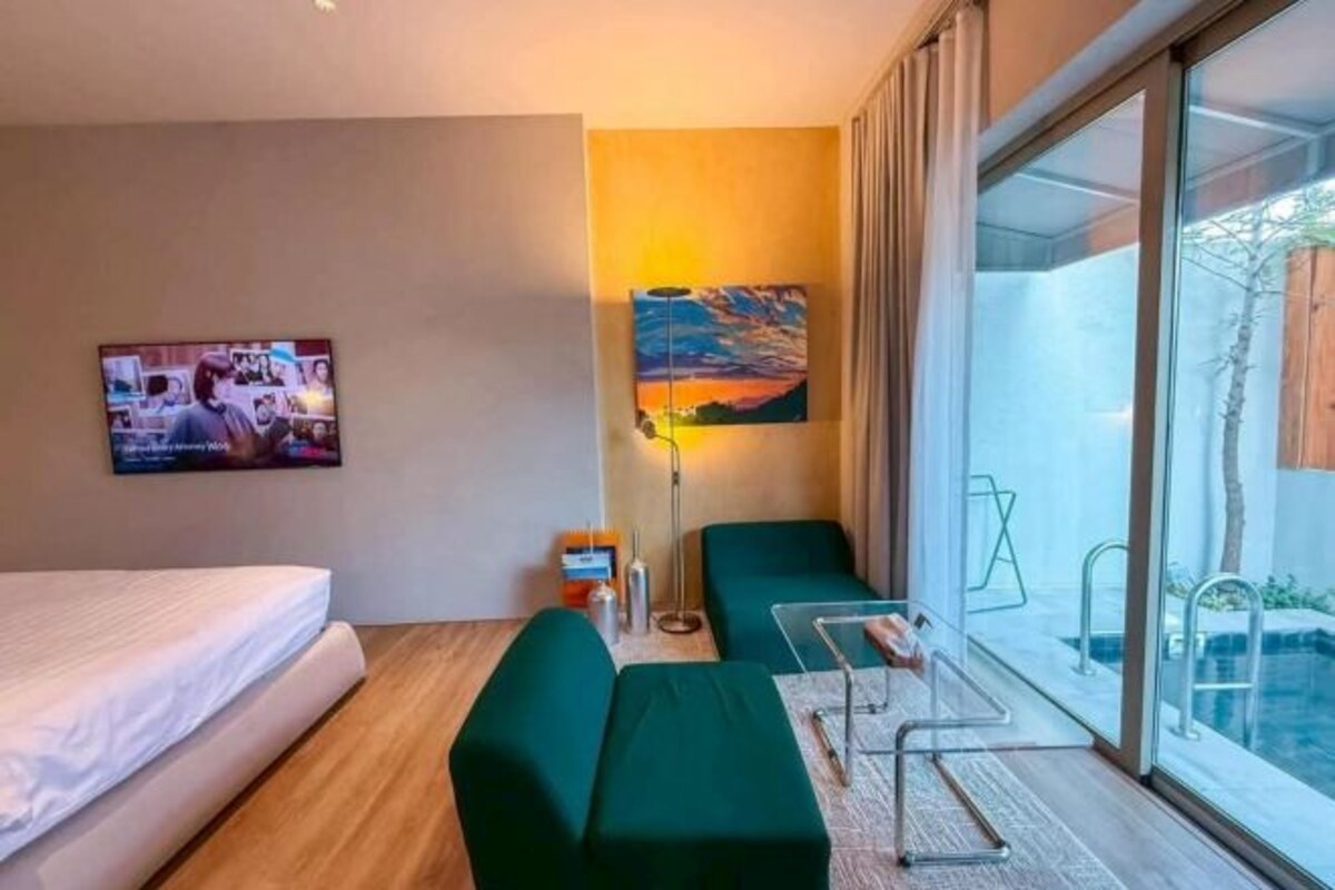 Ein Hotelzimmer mit Bett, einer Sitzecke, einem Fernseher, einem Gemälde und Blick auf einen Swimmingpool.