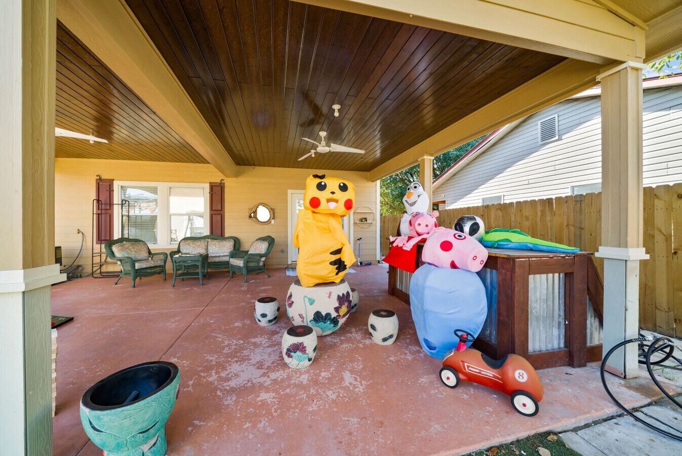 Uma área de varanda coberta com ventilador de teto, móveis de exterior e diversos brinquedos e decorações infantis.