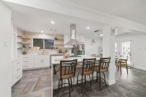 Une cuisine moderne avec des meubles blancs, un îlot central doté de tabourets et une grande cuisinière.