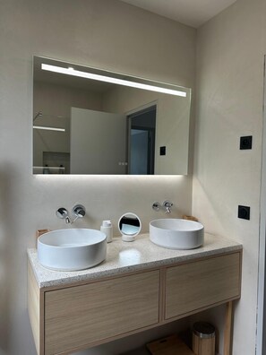 Une salle de bain avec deux lavabos blancs, un grand miroir et un meuble-lavabo en bois.