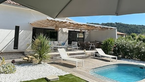 A poolside area with lounge chairs, a covered seating area, and a view of the surrounding landscape.