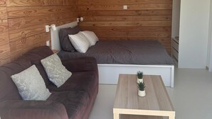 A modern living room with a wooden wall, a sofa, a bed, and a coffee table.