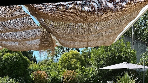 A wooden deck with lounge chairs, a pool, and a shaded area with a net canopy.