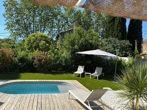 Une terrasse en bois avec une piscine, deux chaises longues et un grand parasol.