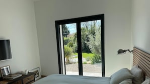 A bedroom with a bed, a TV, a desk with a lamp, and a view of a garden through a sliding door.