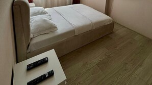 Ein Schlafzimmer mit einem Bett, einem an der Wand montierten Fernseher und zwei Fernbedienungen auf einem kleinen Tisch.