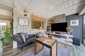 A living room with a black leather sofa, a coffee table, a flat-screen TV, and a bookshelf.