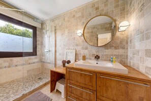 Un baño con un espejo grande, un tocador de madera, una ducha y vistas al exterior.