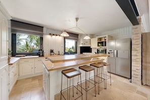 A modern kitchen with a large island, bar stools, a refrigerator, and a view of the outdoors.