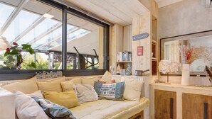 Ein gemütliches Zimmer mit großem Fenster, einer gepolsterten Bank, Holzschränken und einem Bücherregal.