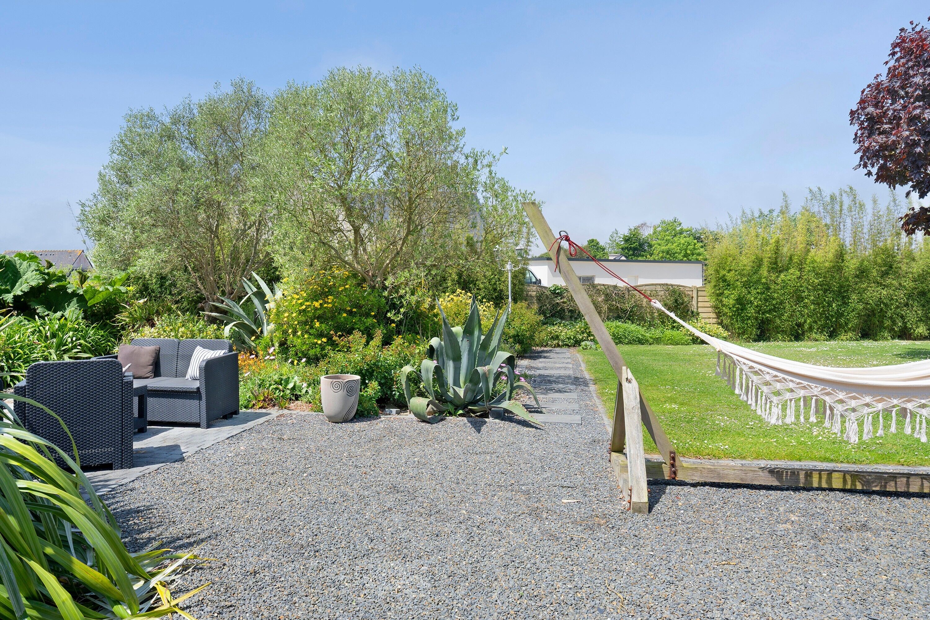 A garden patio with a hammock, outdoor furniture, and a variety of plants.