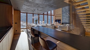 A modern kitchen with a long island, wooden cabinets, and a large window overlooking a snowy landscape.