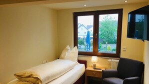Une chambre d’hôtel comprenant un lit, une table de chevet, une chaise et une fenêtre donnant sur des immeubles et des arbres.