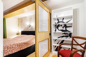 Een slaapkamer met een bed, een houten hoofdbord, een boekenkast met zwart-wit kunstwerken en een rode stoel.