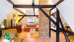 Ein Loft-Zimmer mit freiliegenden Holzbalken, einer Ziegelsteinsäule, einem karierten Sofa und einer Essecke mit Tisch und Stühlen.