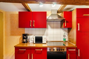 Une cuisine avec des placards rouges, un four à micro-ondes, une machine à café et une cuisinière.