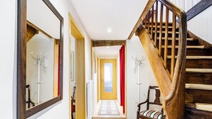 Ein Flur mit einer Holztreppe, einem Spiegel, einem roten Vorhang und einem Stuhl mit einem gestreiften Kissen.